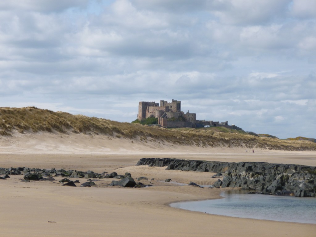 Photo of Bamburgh Castle with beach and rocks in foreground.